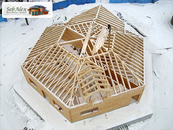 Holzhaus im Bau; Dachstuhl sichtbar, umgeben von Schnee.