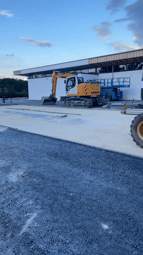 Ein gelber Bagger steht vor einem im Bau befindlichen Gebäude.
