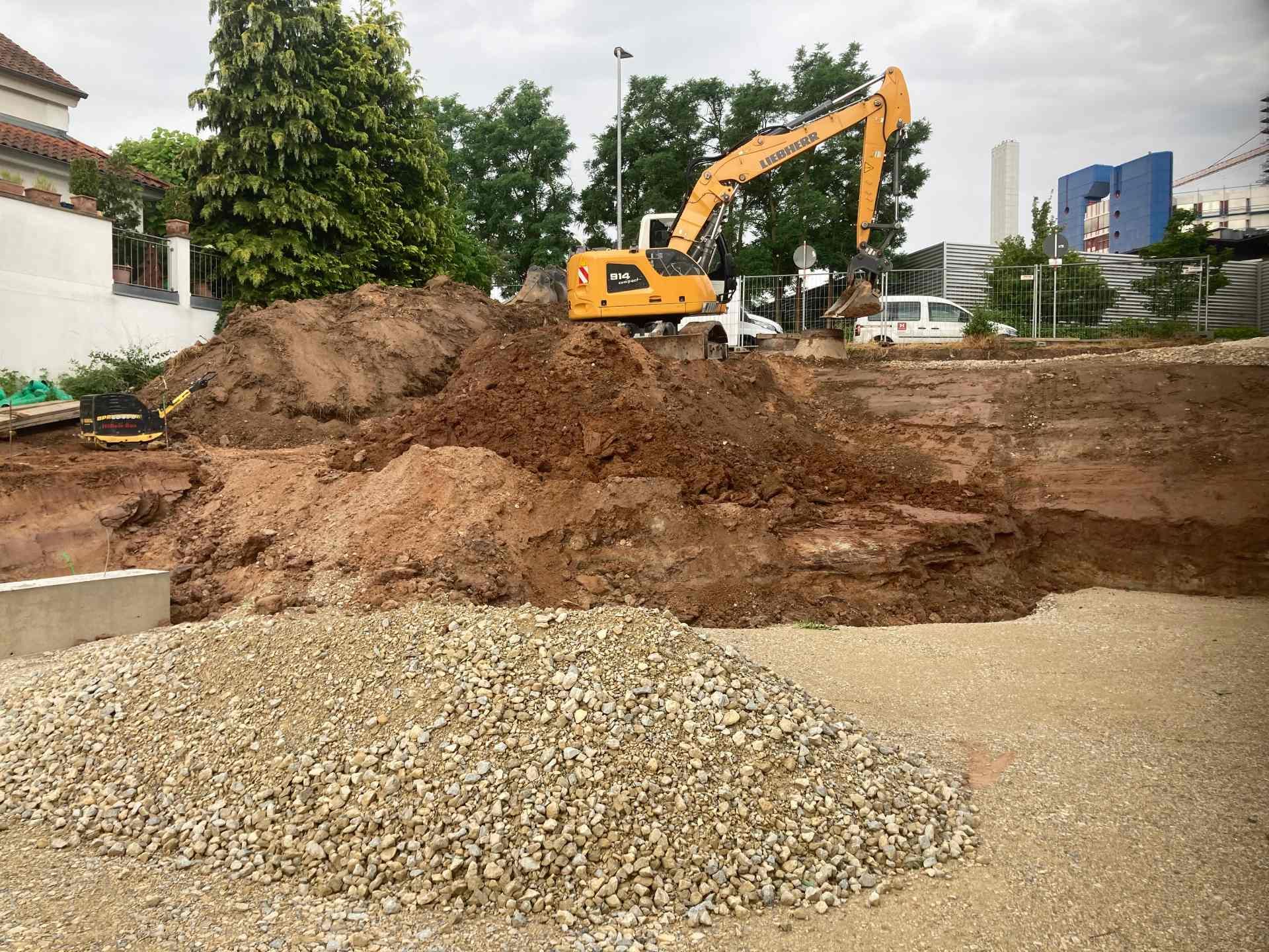 Ein gelber Bagger gräbt ein Loch in einen Kieshaufen.