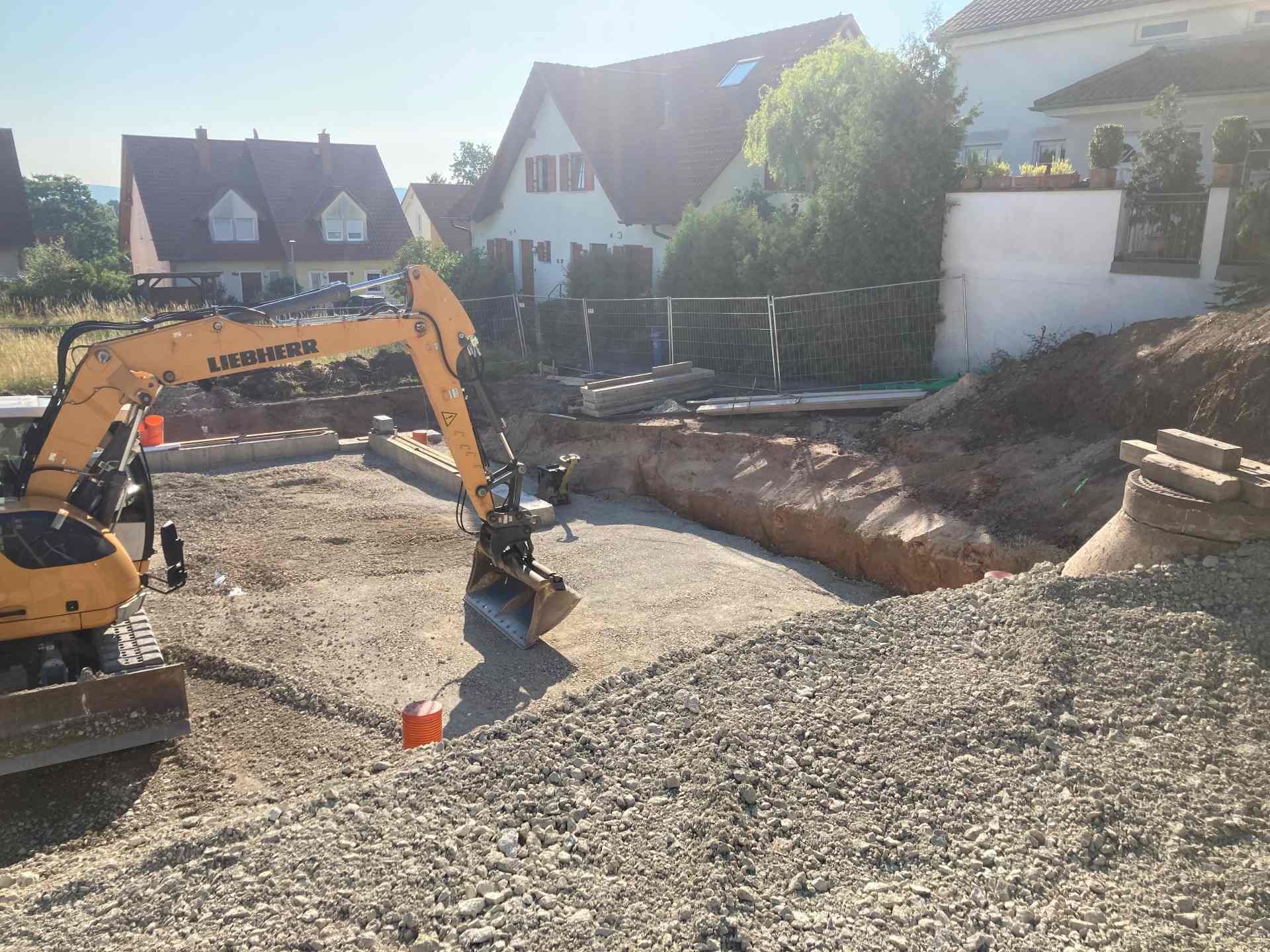 Ein gelber Bagger arbeitet auf einer Baustelle vor einem Haus.