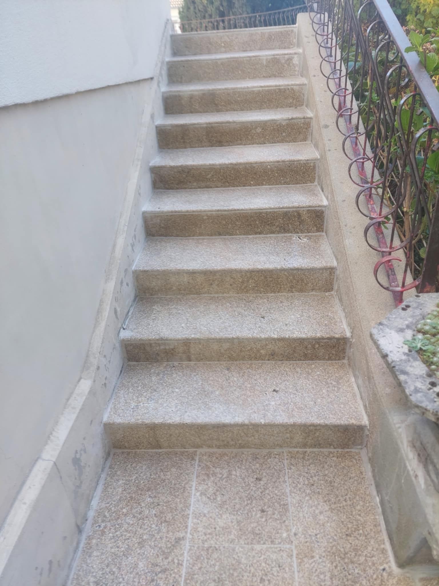 Escalier en pierre montant, avec une rampe à droite et un mur à gauche.