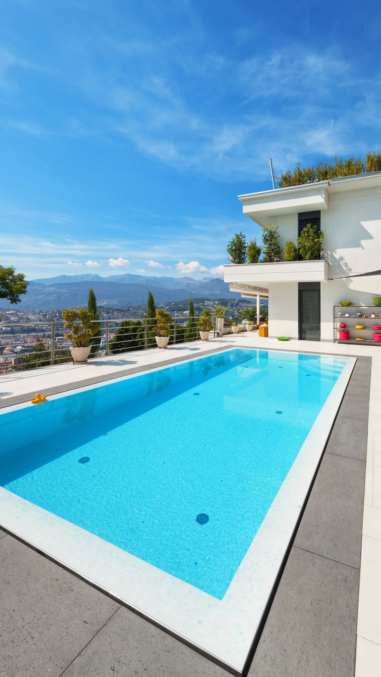 Piscine avec une margelle en granit sur la terrasse d'une maison blanche