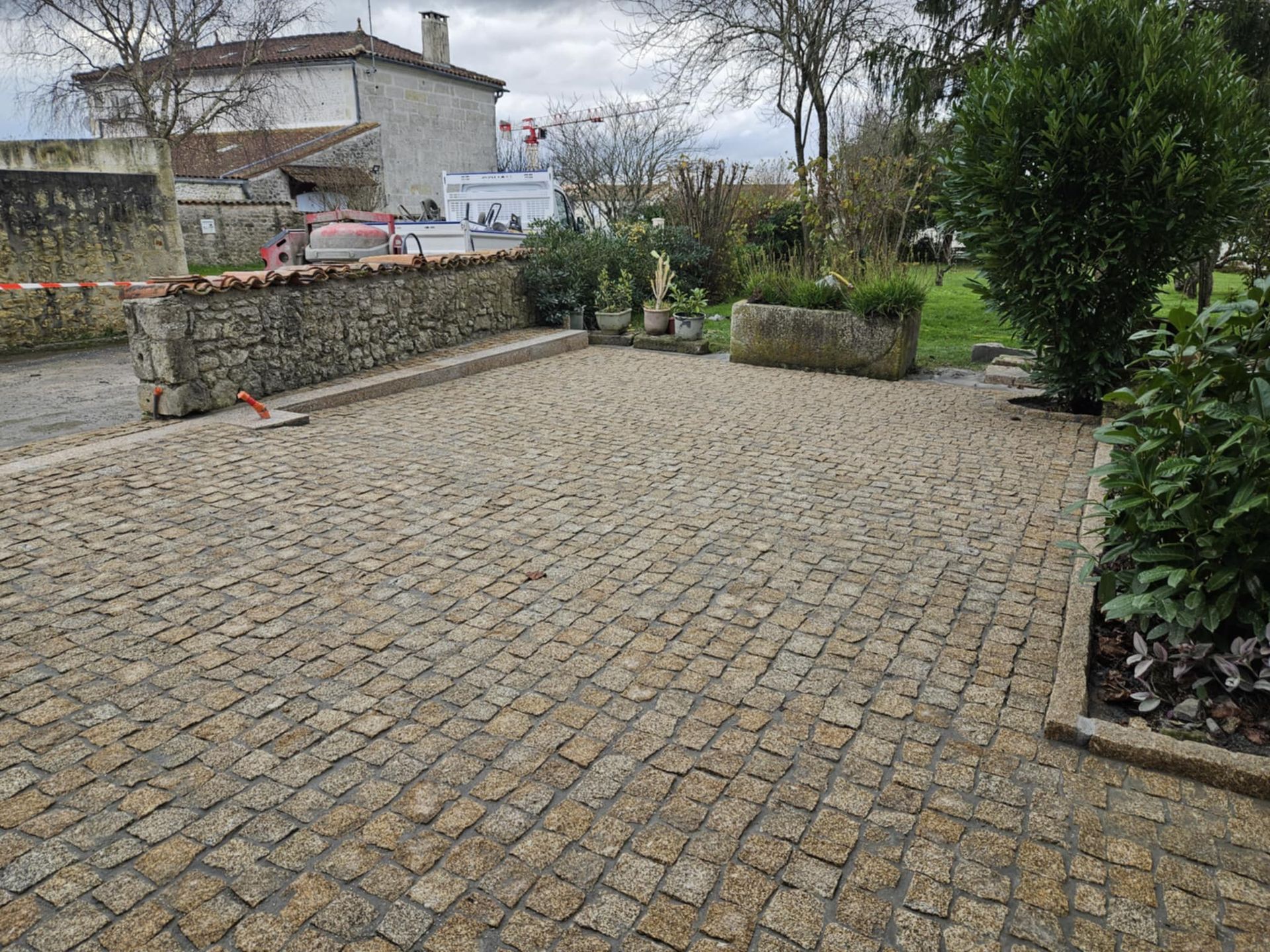 Cour pavée avec un muret en pierre, une jardinière et un bâtiment en arrière-plan.