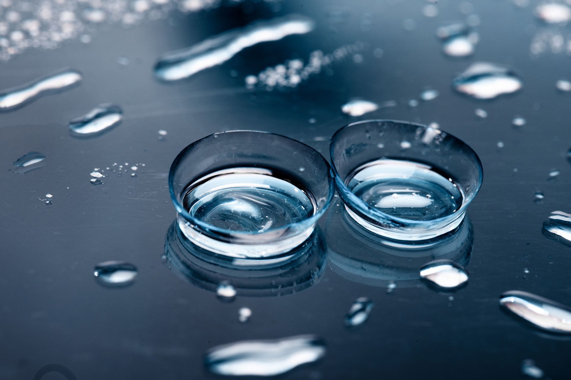 Dos lentes de contacto están sobre una superficie húmeda rodeadas de gotas de agua.