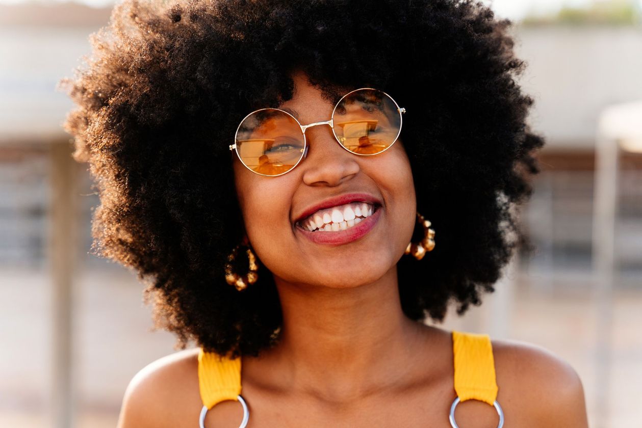 Una mujer con afro lleva gafas de sol y sonríe.
