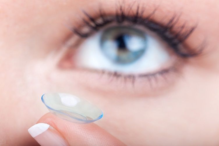 Una mujer se pone una lente de contacto en el ojo.