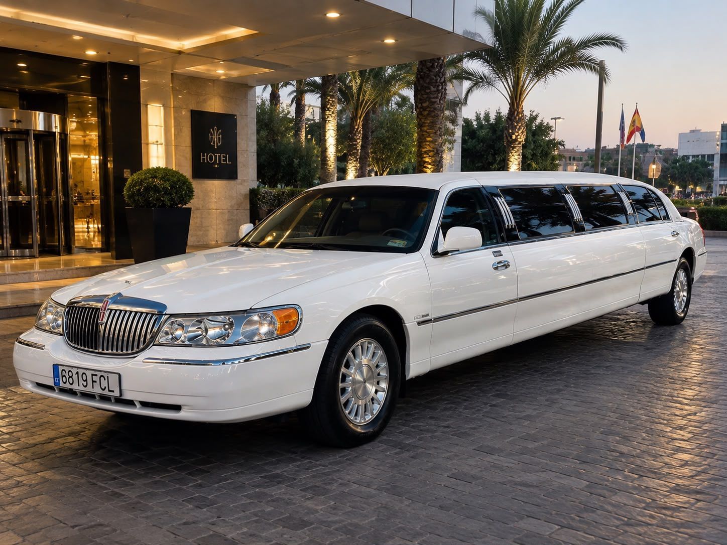 Limusina blanca alargada aparcada a la entrada de un hotel al anochecer