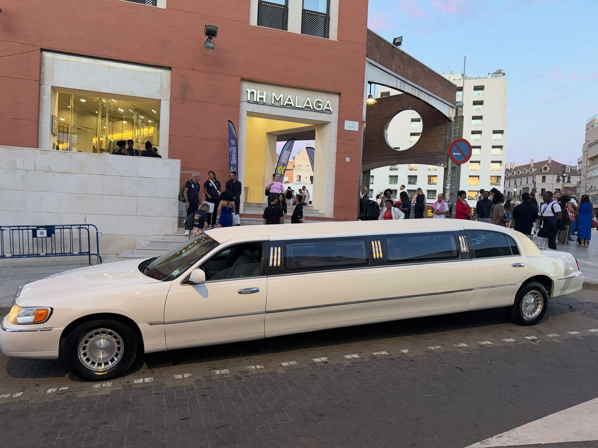 Limusina blanca alargada estacionada frente a un edificio de ladrillo rojo, con gente reunida cerca