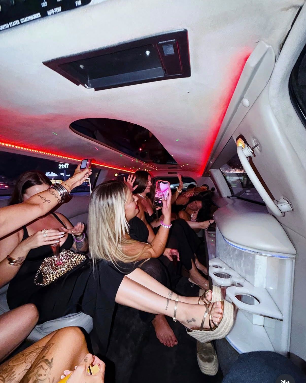 Personas sentadas en un club limusina, con luces rojas en el techo y bebidas, haciéndose fotos dentro del vehículo