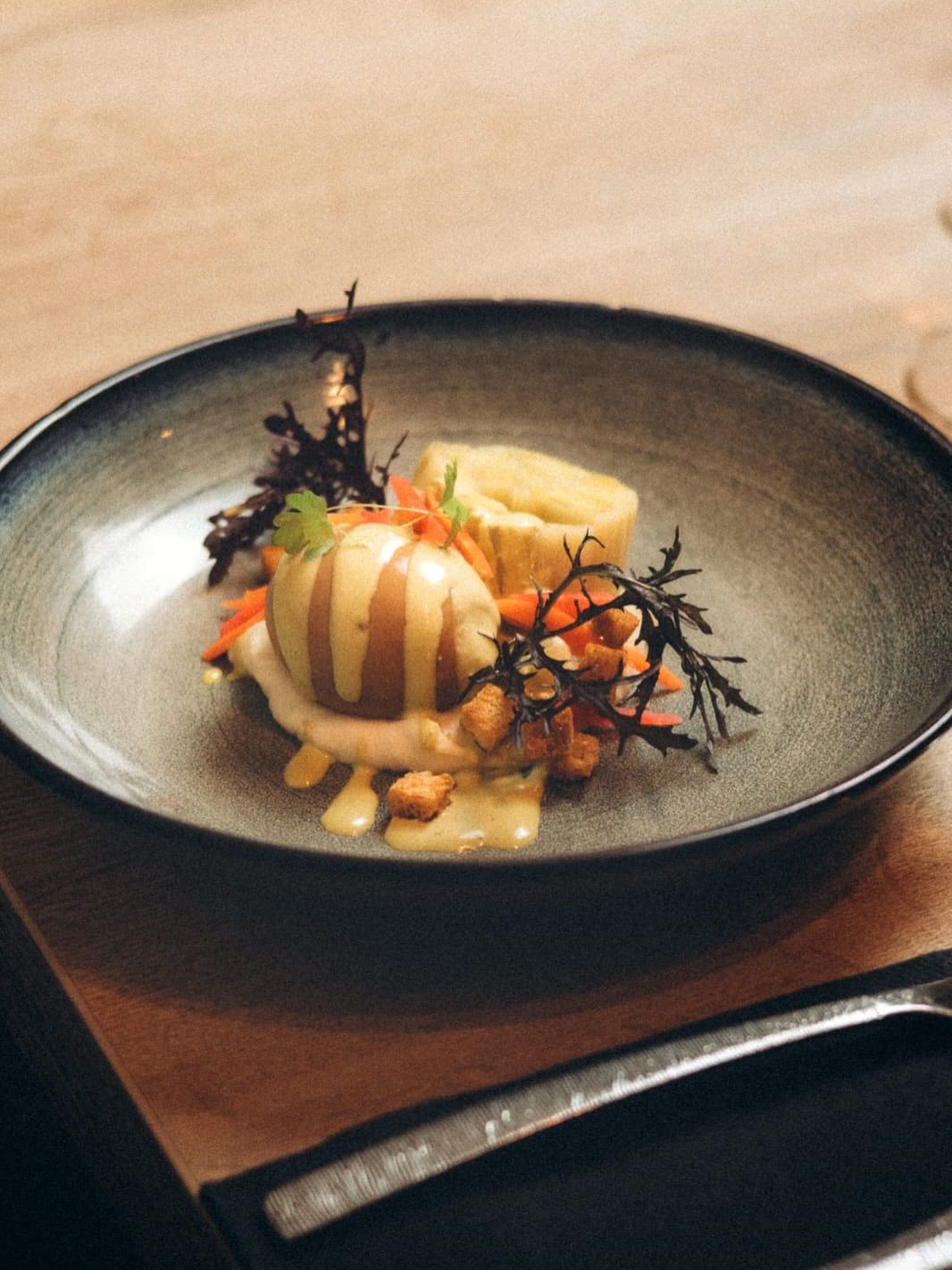 Dessert servi à l'assiette, nappé de caramel et garni de baies et de menthe, sur une table en bois.