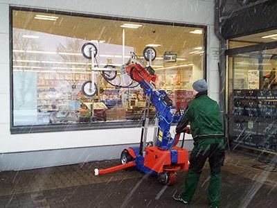 Ein Mann hebt mit einer Maschine ein Glasfenster aus dem Schnee an.