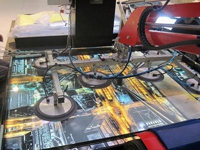 Eine Maschine hebt ein Stück Glas mit dem Bild einer Stadt darauf an.