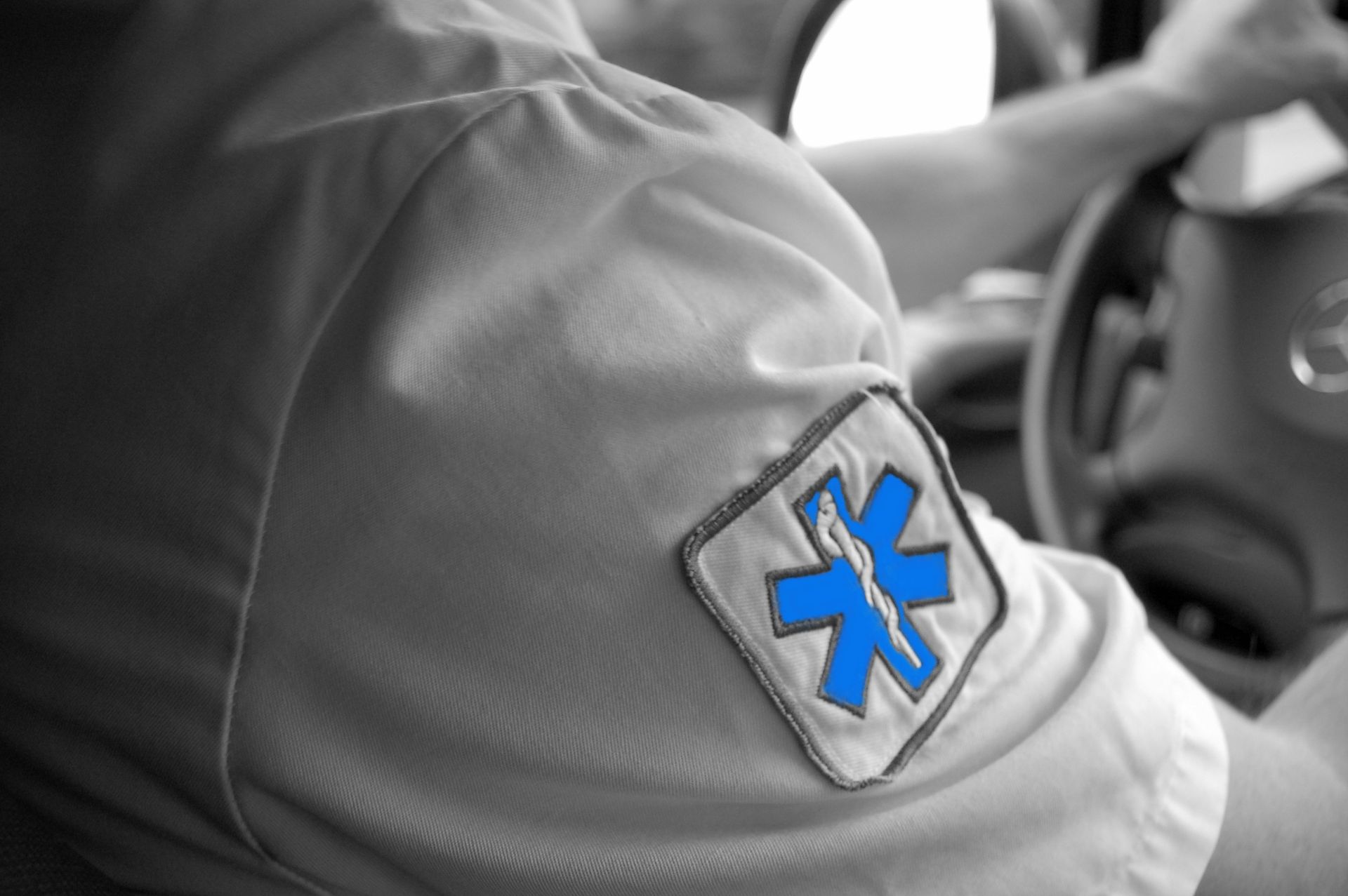 Un ambulancier au volant d'une ambulance, portant une chemise avec un écusson bleu en forme d'étoile de vie.
