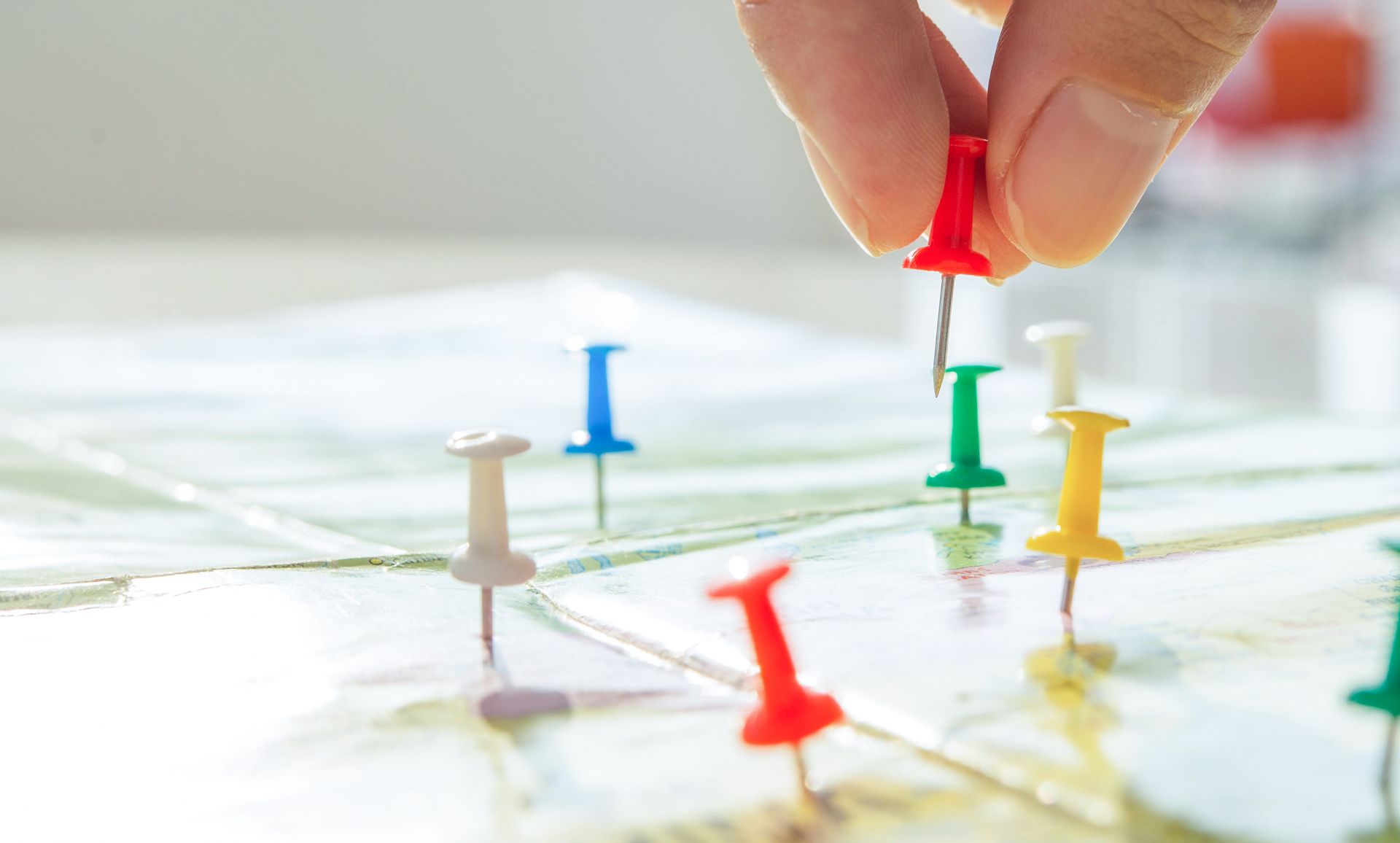 Une main place une punaise rouge sur une carte entourée de plusieurs punaises de couleurs différentes.