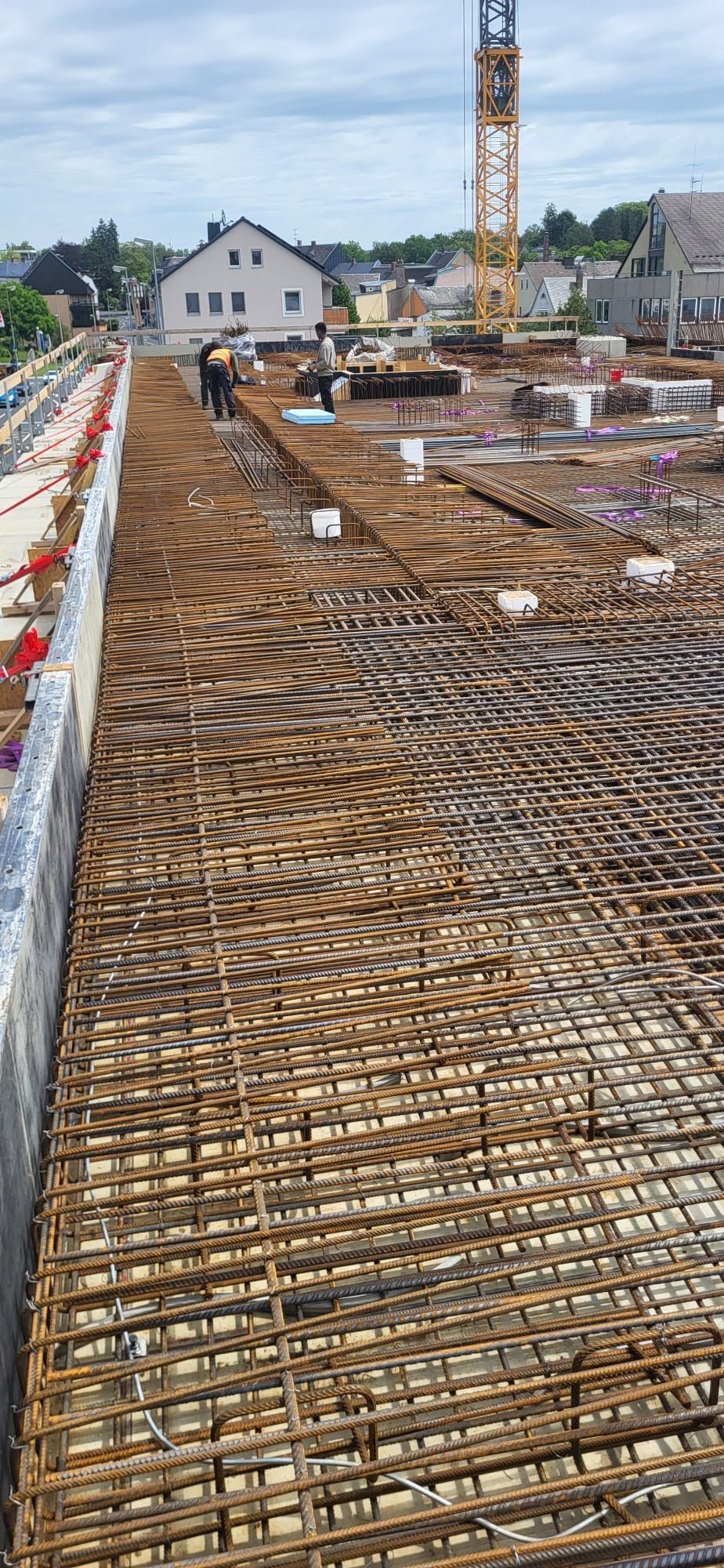 Baustelle mit Stahlbewehrungsfundament und Arbeitern in der Ferne unter einem Kran.