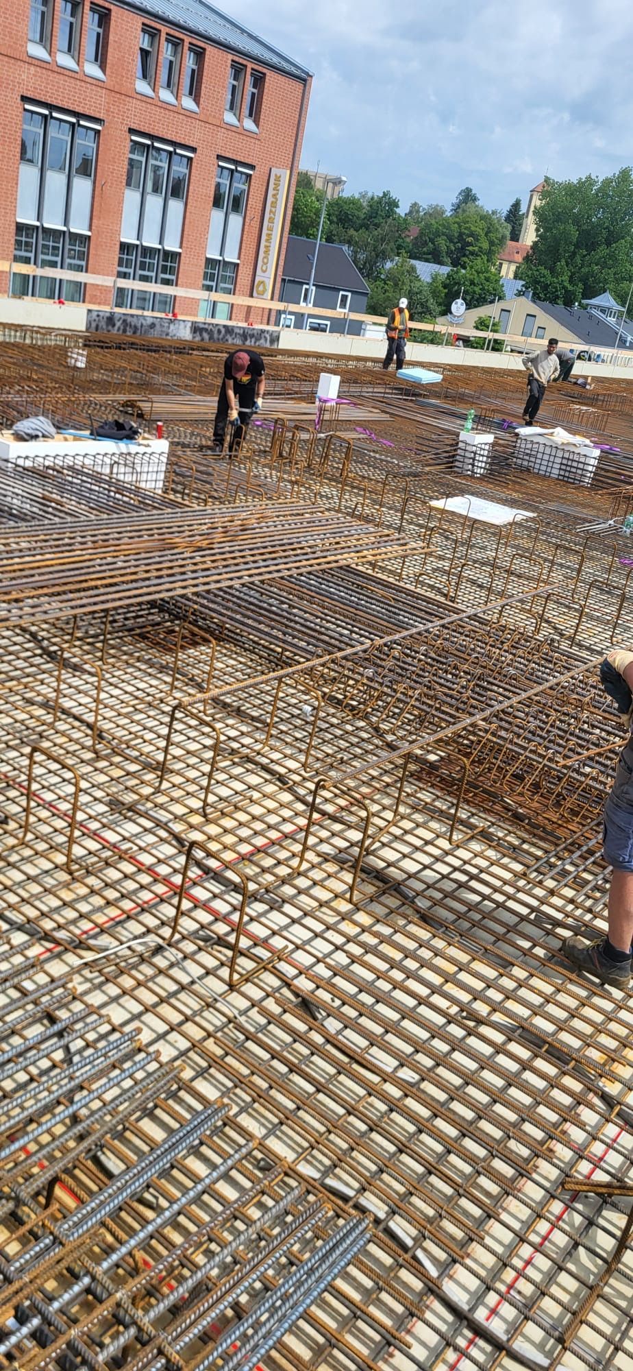Baustelle mit Stahlbewehrungsgitter und Arbeitern in der Nähe eines roten Backsteingebäudes