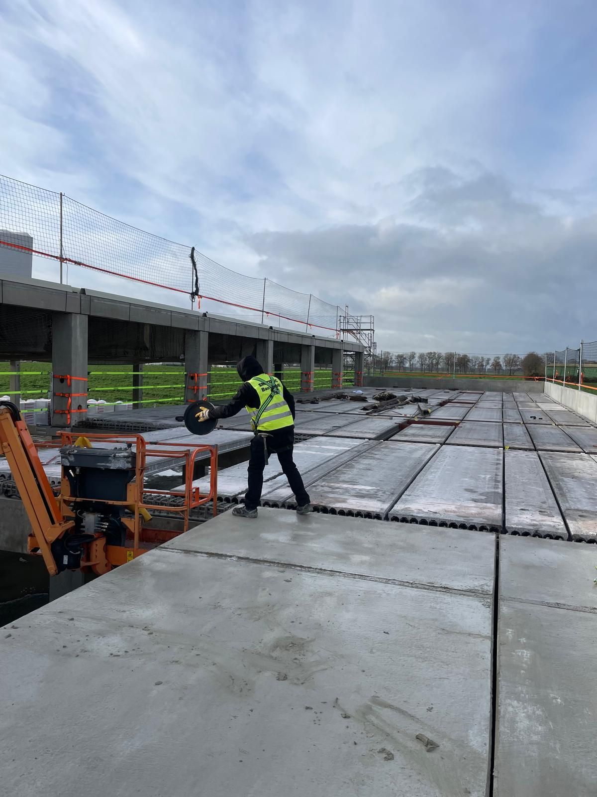 Bauarbeiter in Sicherheitsweste auf Betonplatten in der Nähe eines Gebäudes.