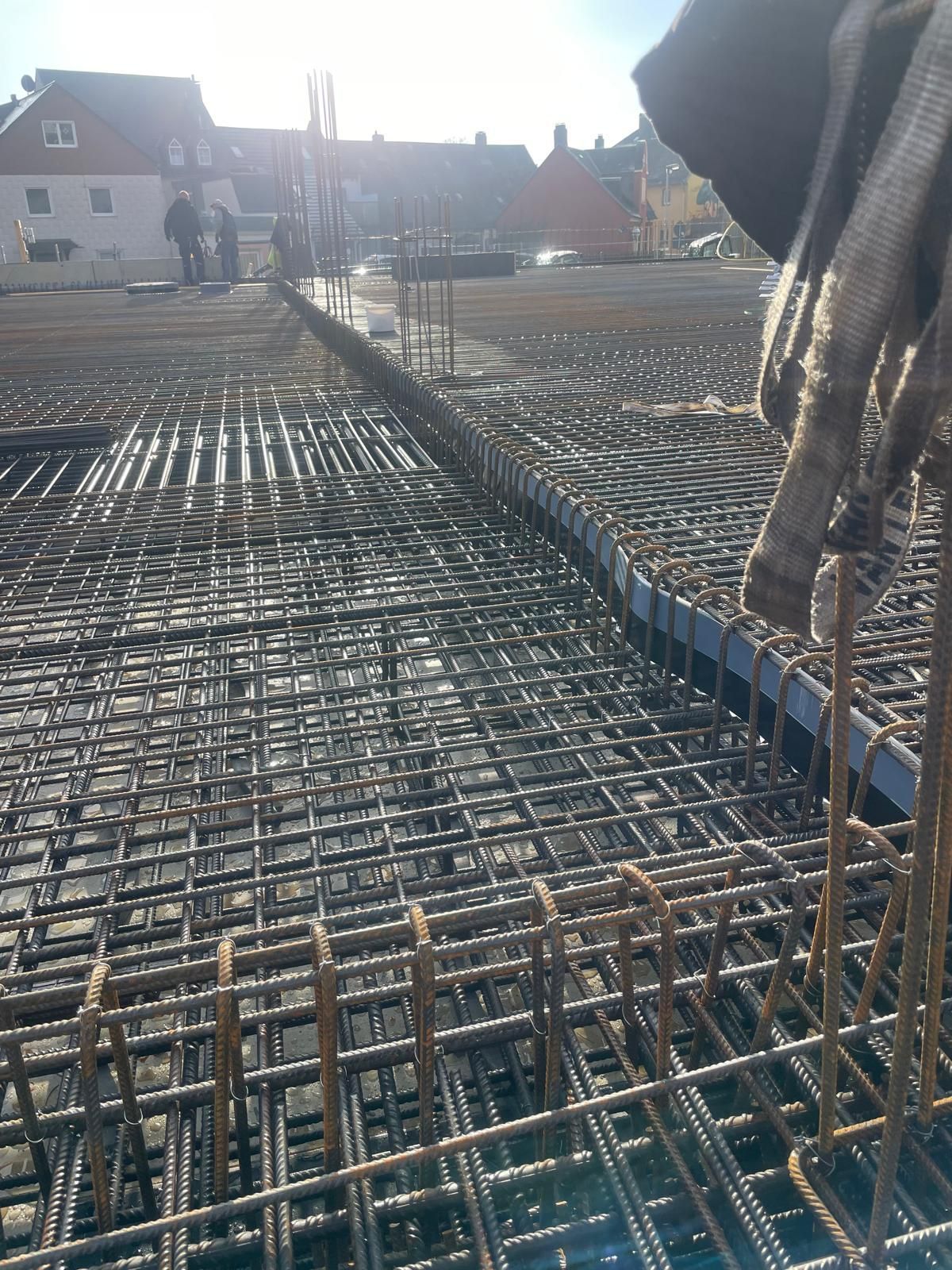 Stahlbetonfundament für eine Baustelle. Arbeiter und Gebäude im Hintergrund.