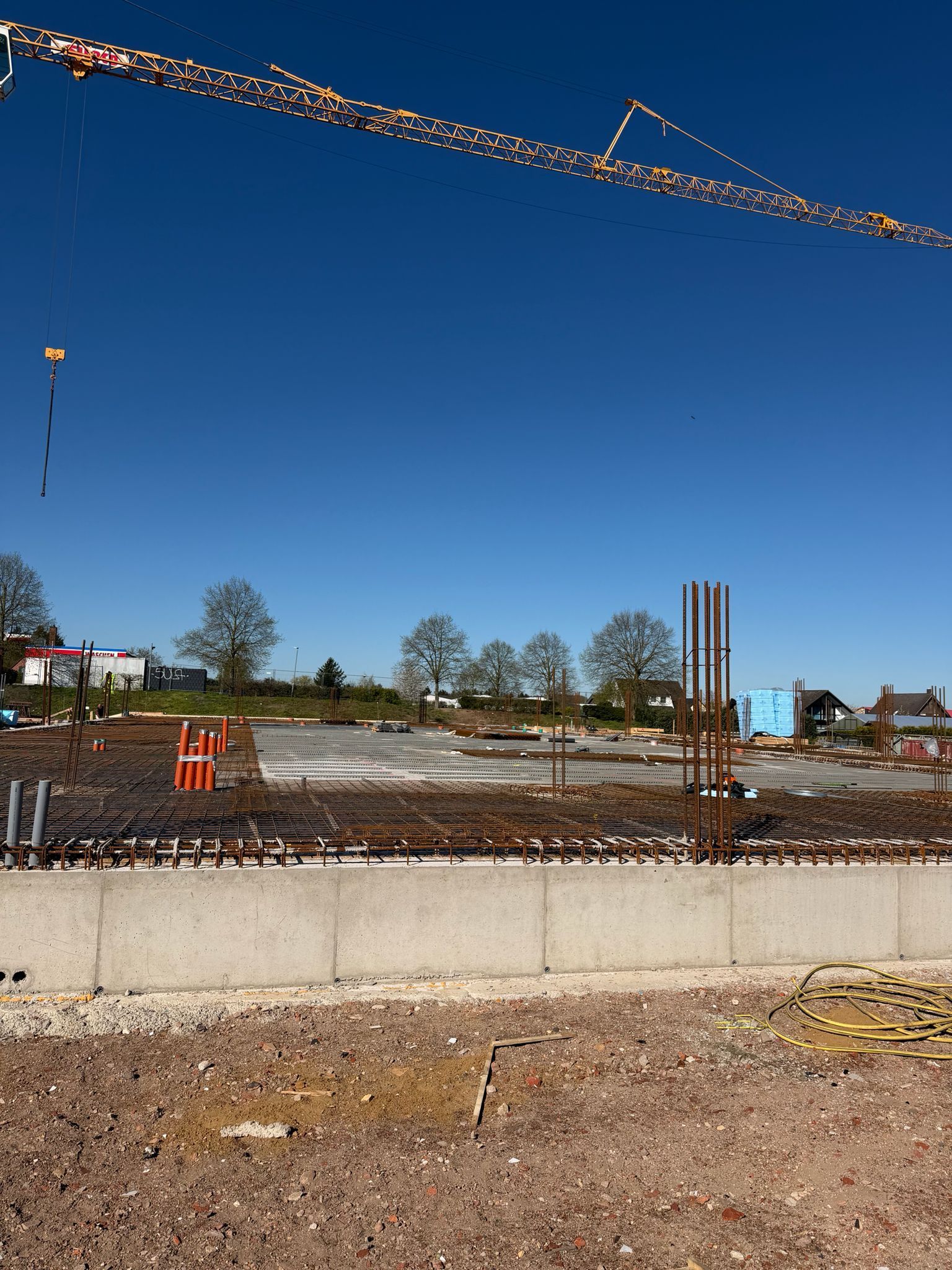 Baustelle mit Kränen und Bewehrungsstahl unter strahlend blauem Himmel