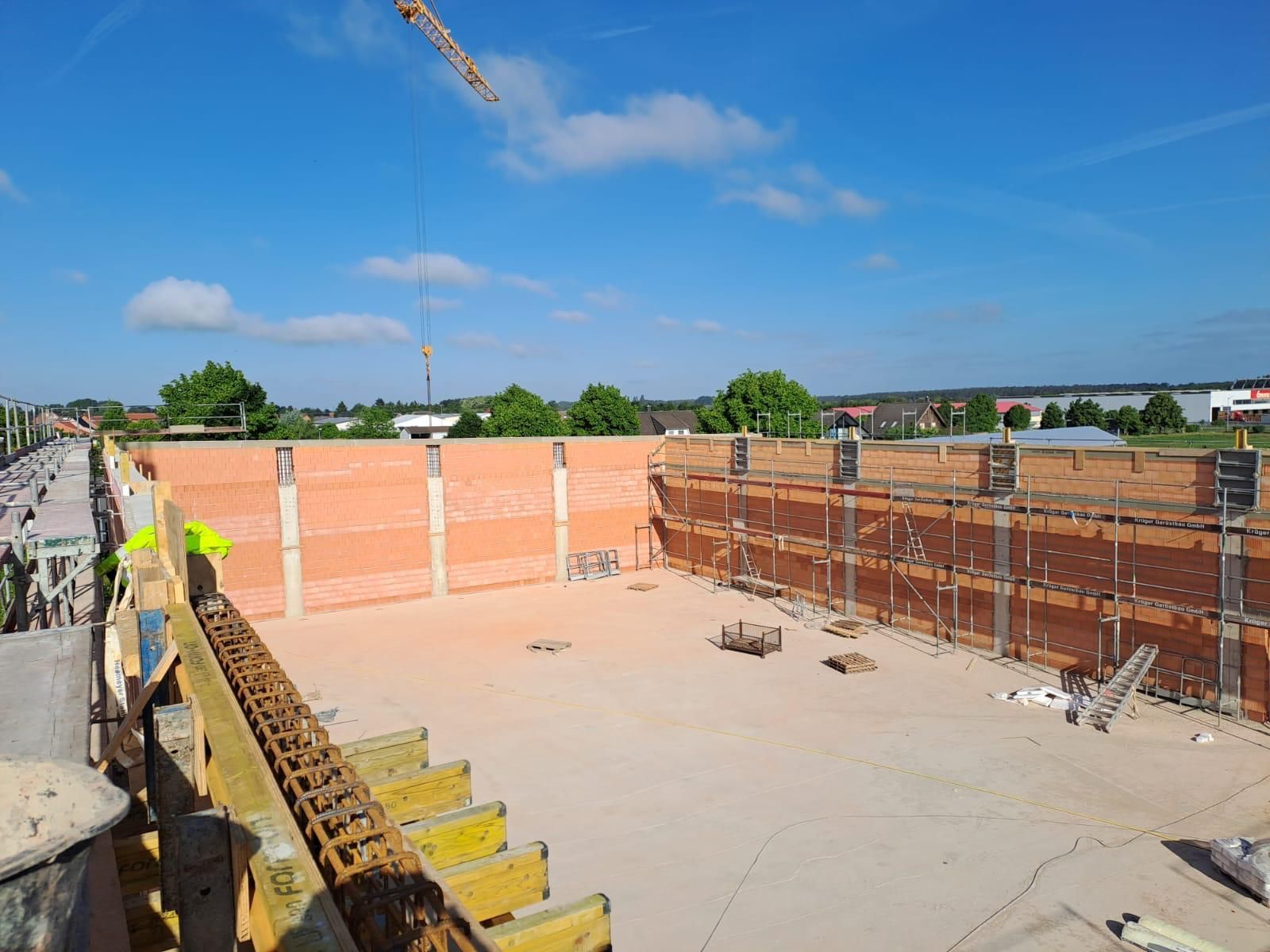 Baustelle mit Betonfundament, Ziegelwänden, Bewehrungsstahl und Arbeitern in Sicherheitswesten unter blauem Himmel
