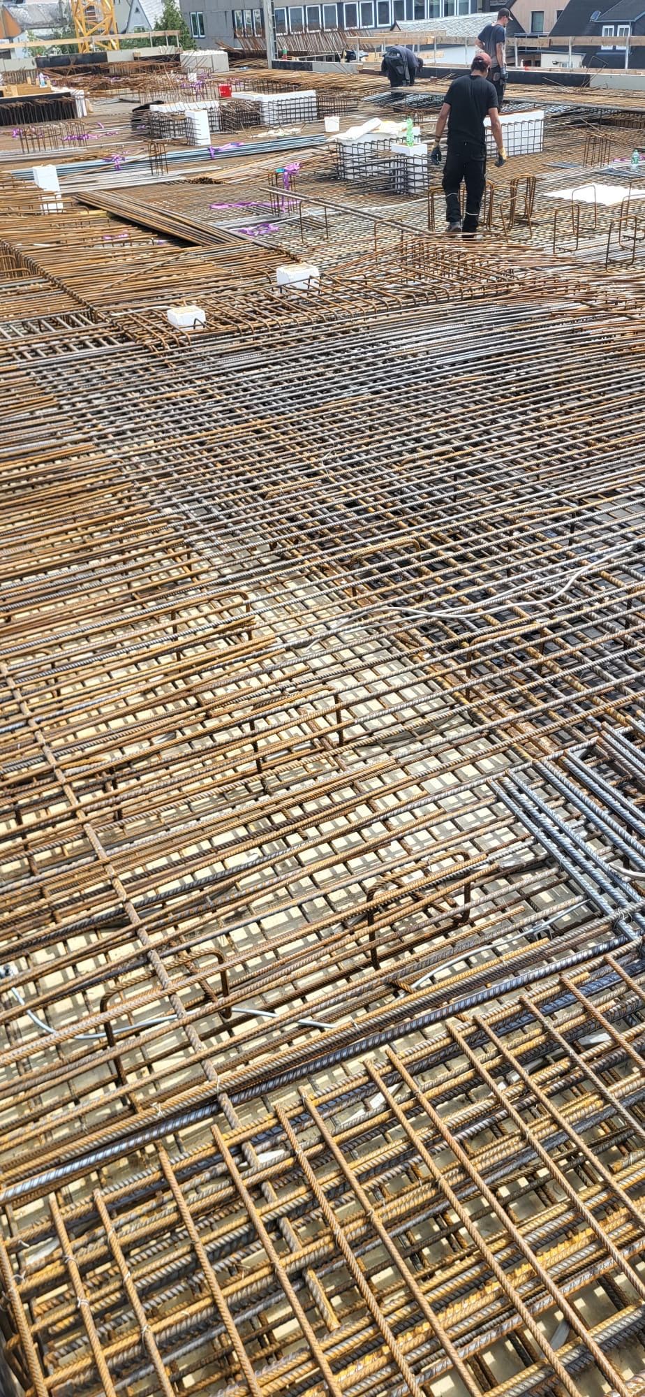 Baustelle mit großem Stahlbeton-Gitterfundament und einem im Hintergrund stehenden Arbeiter.