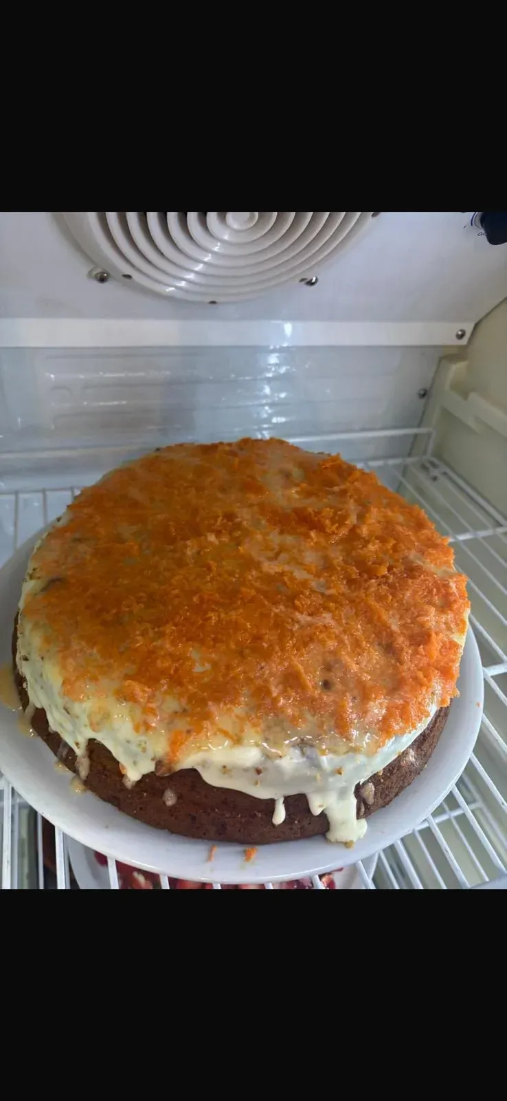 Pastel redondo con glaseado de naranja en el refrigerador, con glaseado blanco goteando por los lados.