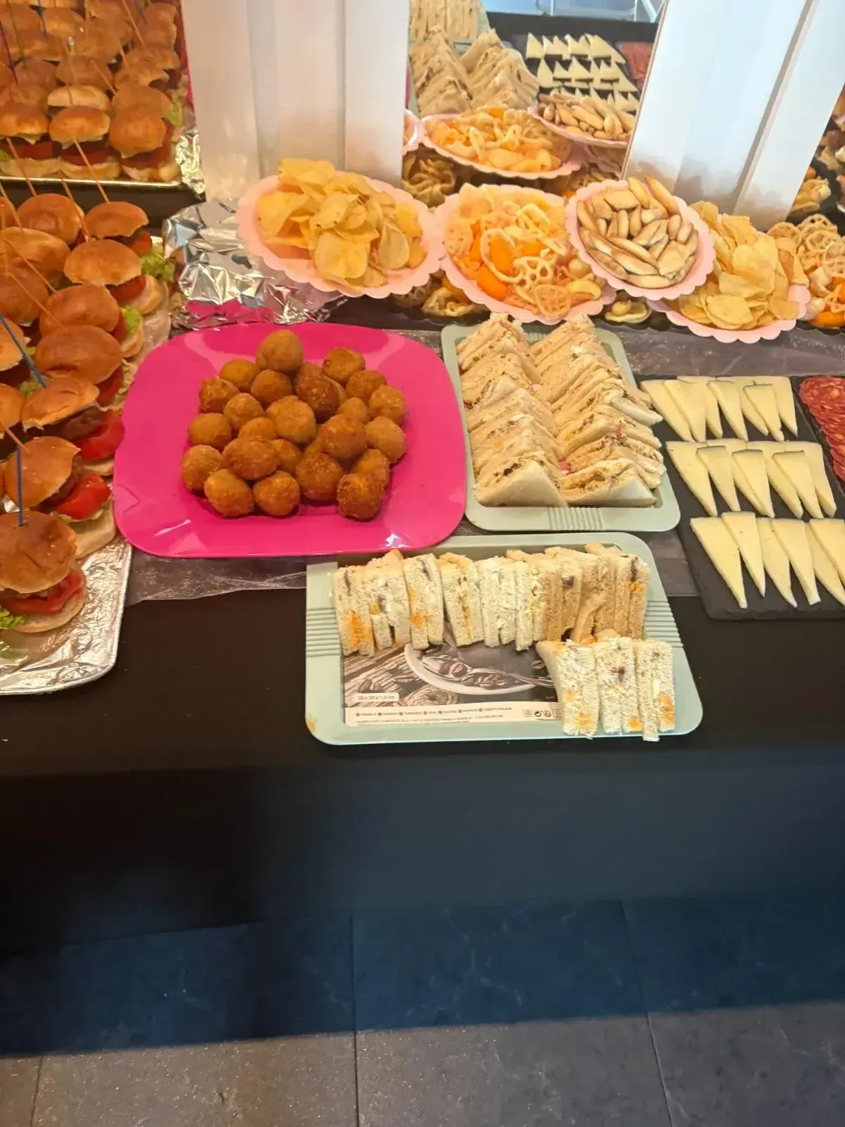 Mesa de buffet con una variedad de pasteles, sándwiches y aperitivos en platos y bandejas.