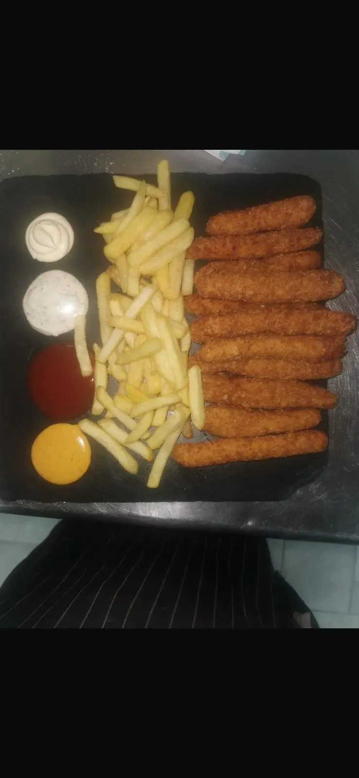 Papas fritas y palitos de pescado empanizados en una bandeja negra con salsas para mojar a la izquierda.