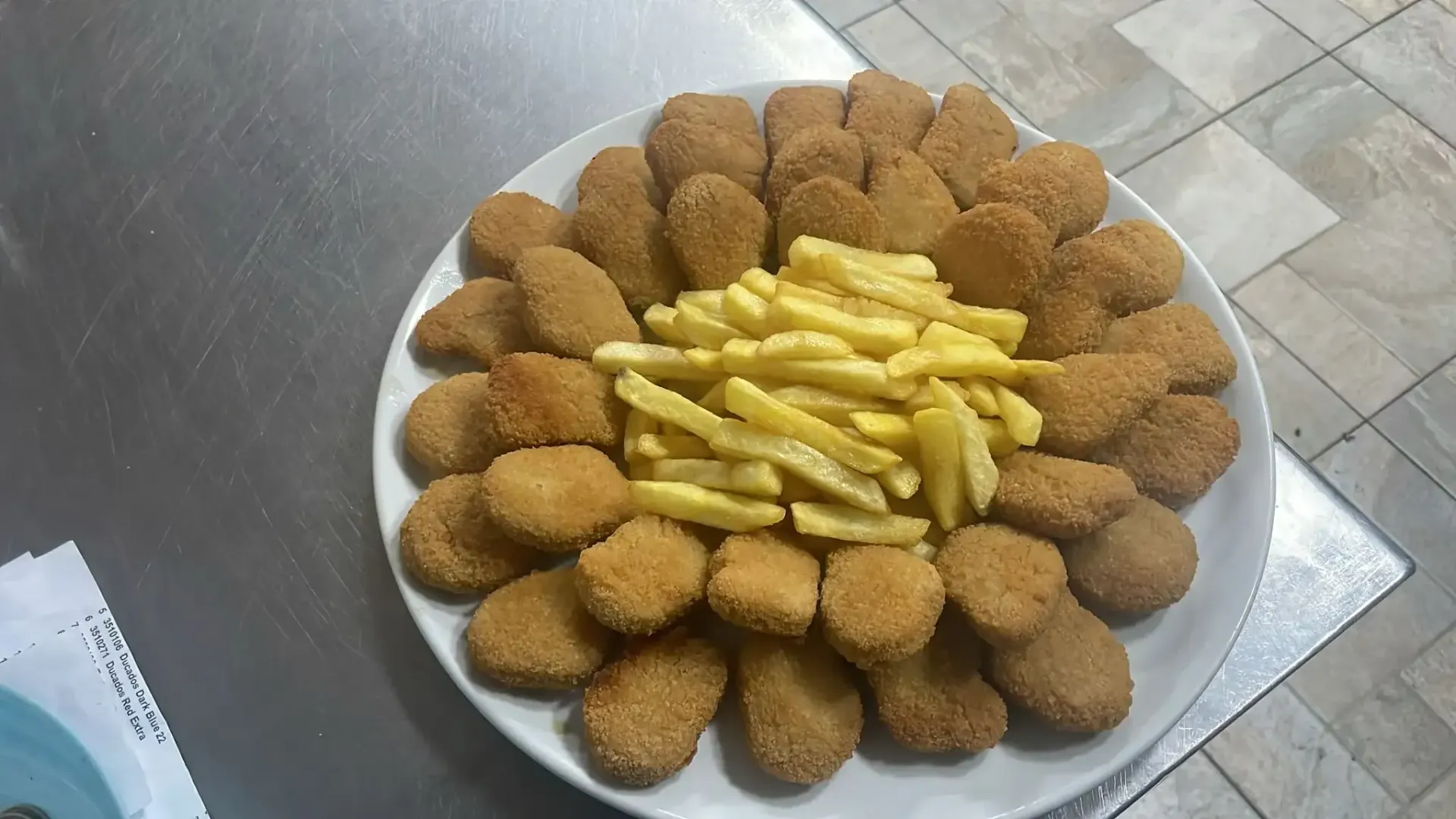 Plato de croquetas empanizadas dispuestas alrededor de una pila de papas fritas sobre un mostrador de metal.