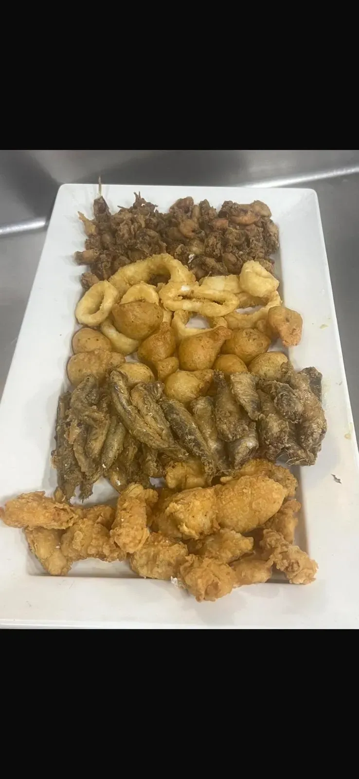 Plato de aperitivos fritos variados, incluyendo camarones, en una fuente rectangular blanca.