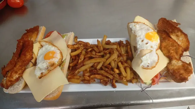 Primer plano de un sándwich de baguette rebanado, relleno con capas de jamón, queso y tomate, servido en un plato blanco.