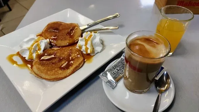Un desayuno que incluye dos tortitas con nata montada y sirope, un vaso de café y un vaso de zumo de naranja.