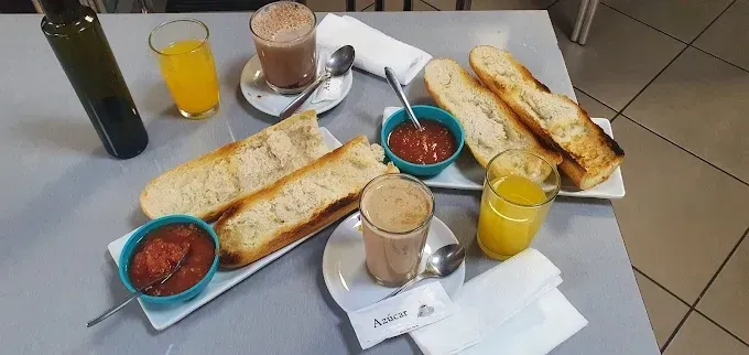 Una mesa puesta para dos con pan tostado, paté de tomate, vasos de zumo de naranja y tazas de café con leche.