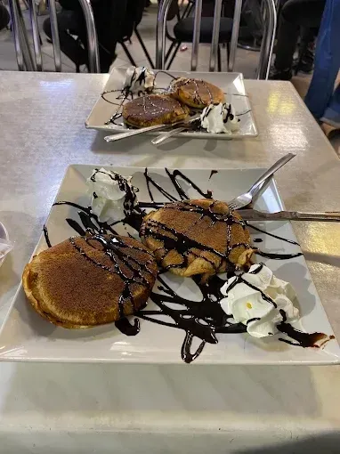 Dos platos de tortitas servidas con salsa de chocolate y nata montada, colocados sobre una mesa en el comedor.