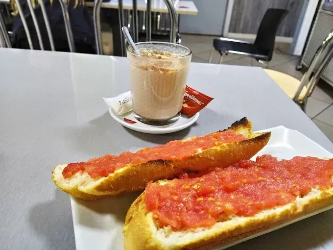 Dos rebanadas de pan tostado con tomate rallado, servidas con un vaso de batido o bebida láctea en la mesa.