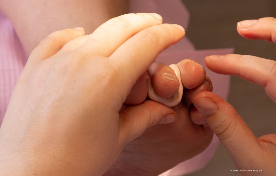 Hände, die in einer sanften, hellen Umgebung auf einem Bett eine Fußmassage geben, während die Füße unbedeckt sind