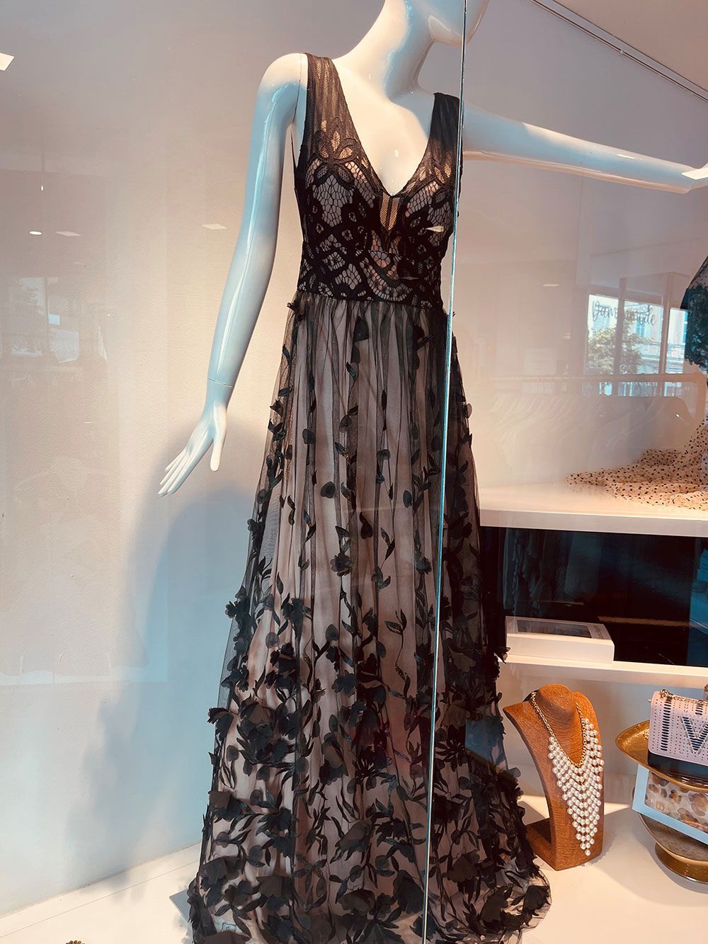 Ein schwarzes Spitzenkleid hängt auf einer Schaufensterpuppe in einem Ladenfenster.