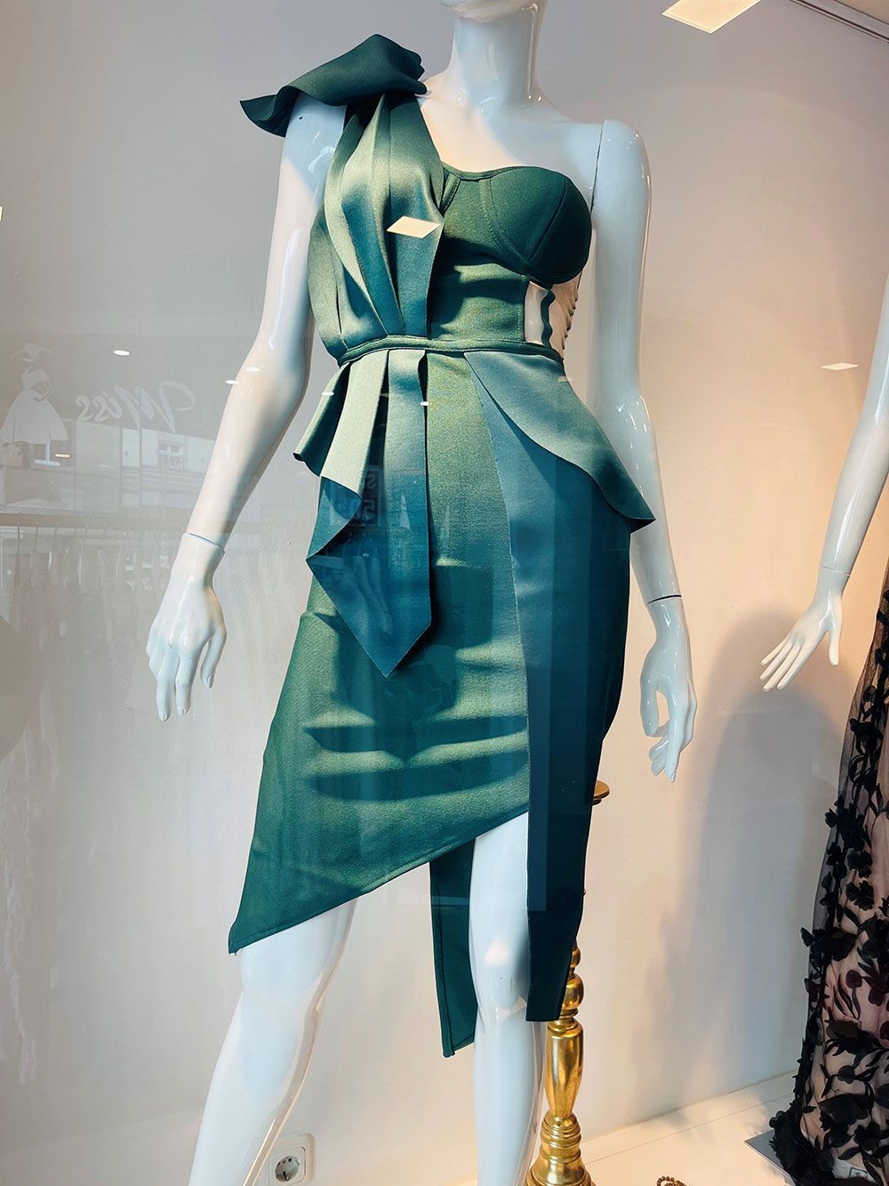 Ein grünes Kleid hängt auf einer Schaufensterpuppe in einem Schaufenster.
