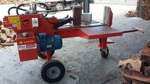 Rachador de lenha vermelho com motor elétrico, rodas e cunha de corte, instalado ao ar livre.