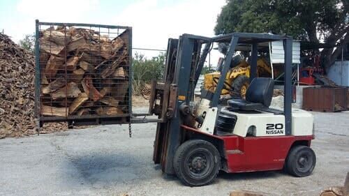 Empilhadeira com carga de lenha, ao ar livre.