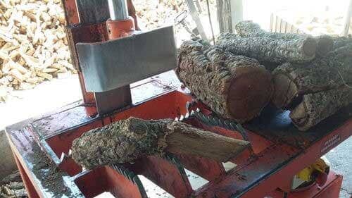 Rachador de lenha rachando um tronco. Máquina laranja com lâmina. Troncos em uma bandeja.