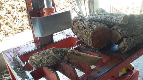 Rachador de lenha com estrutura laranja e lâmina prateada, cortando um tronco texturizado.