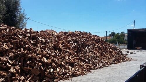Pilha de casca de cortiça marrom em um ambiente industrial sob um céu azul brilhante.