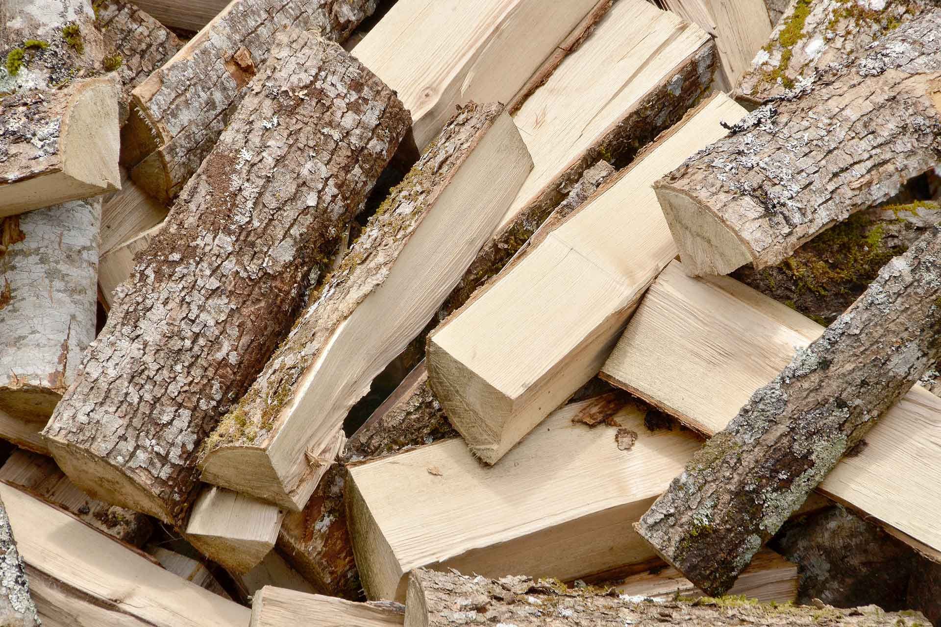 Pilha de lenha rachada, algumas partes com casca, outras de madeira clara.
