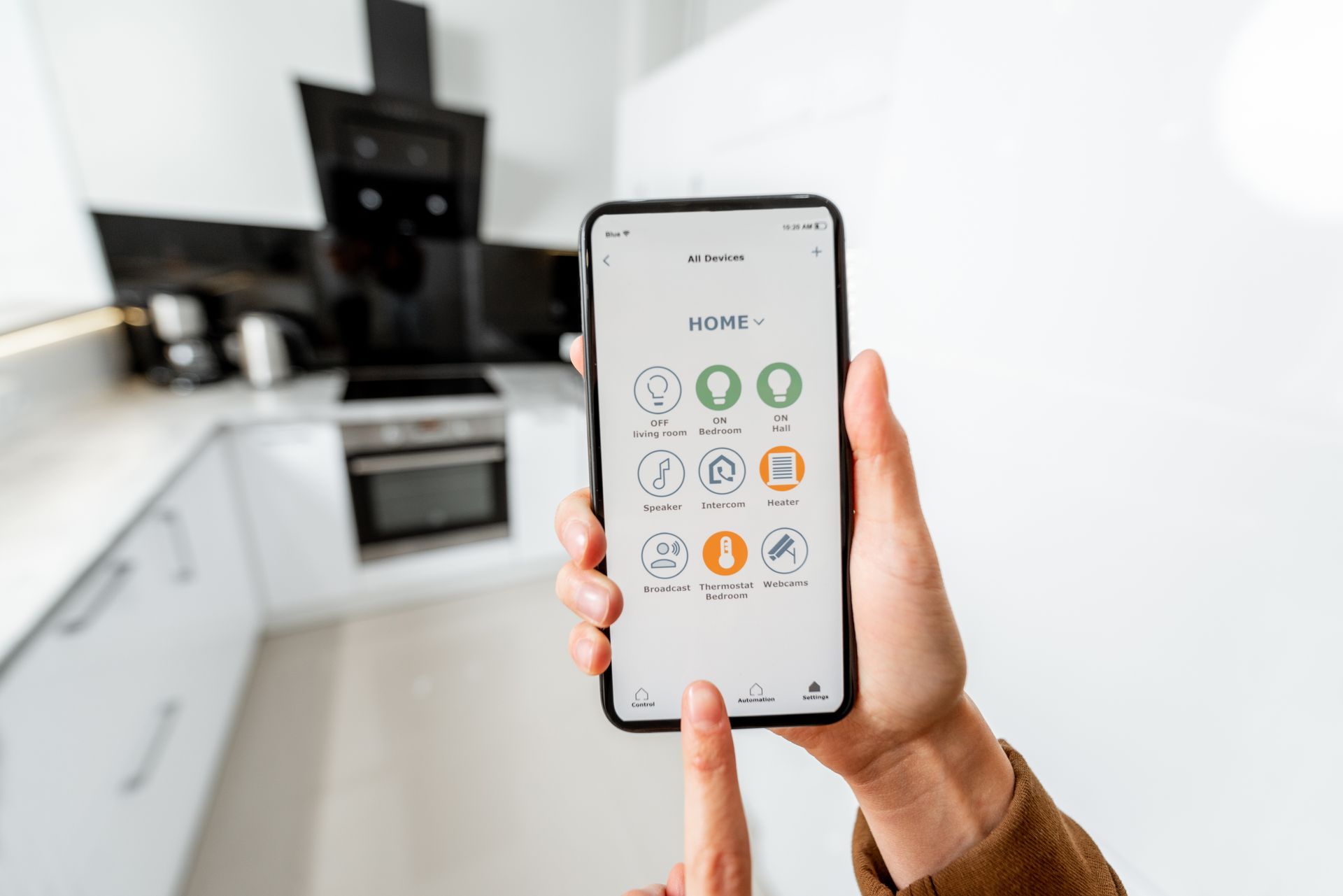 Dans une cuisine moderne, une personne tient un smartphone et utilise une application domotique pour contrôler des appareils connectés.