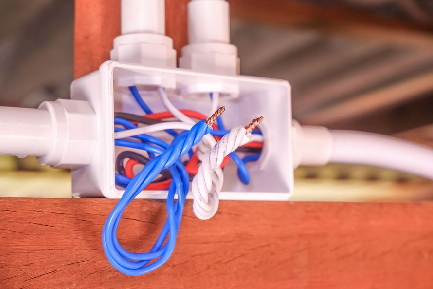 Boîte de jonction électrique ouverte, montée sur du bois, montrant des connexions de fils torsadés et exposés, sans capuchons de sécurité.