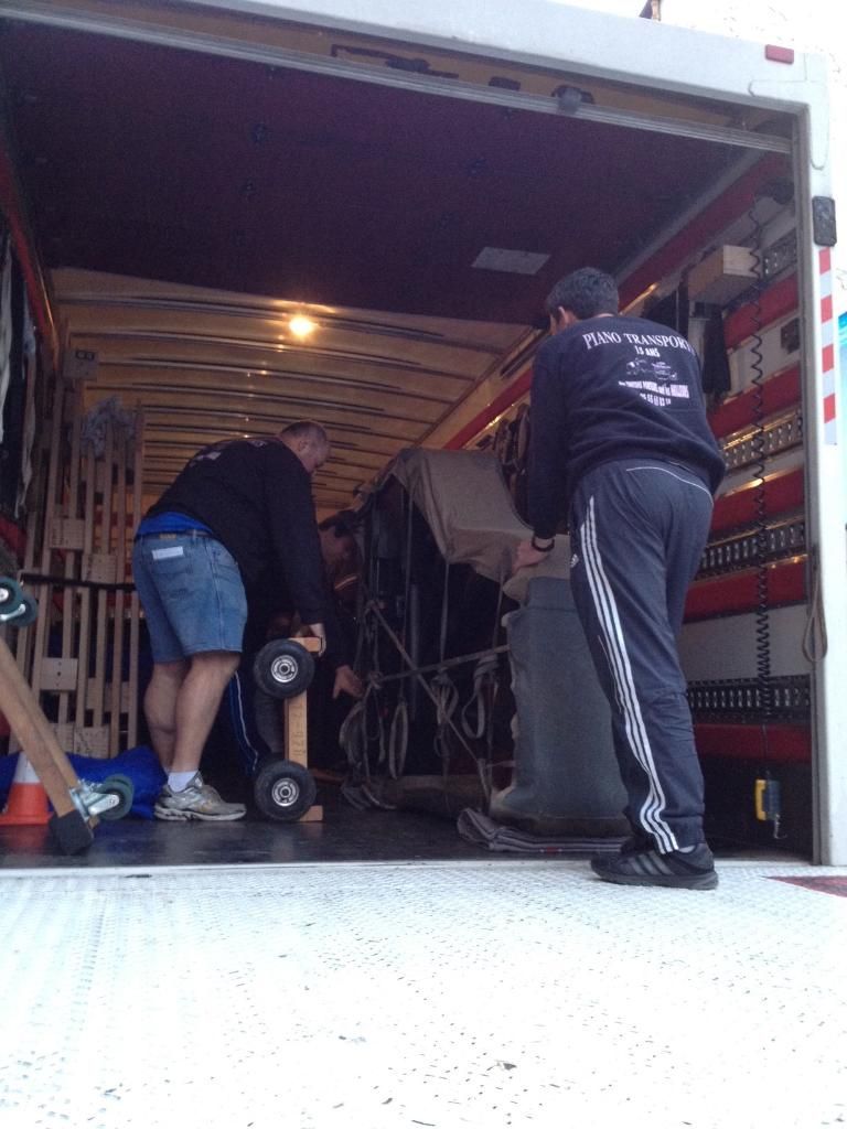 Deux personnes chargent un camion avec des cartons et du matériel à l'intérieur d'une remorque ouverte.