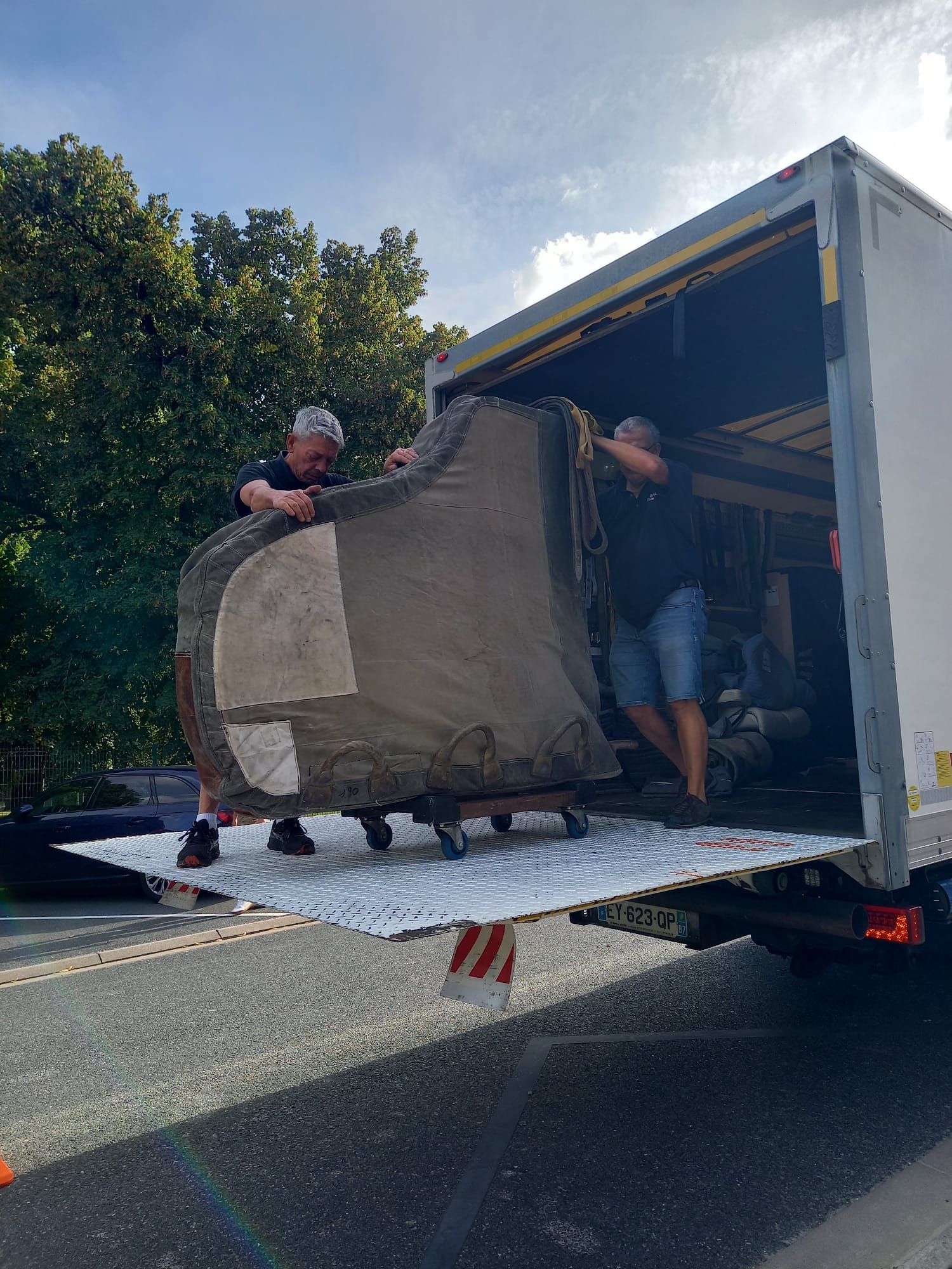 Deux déménageurs déchargent un grand canapé d'un camion blanc en bord de route.