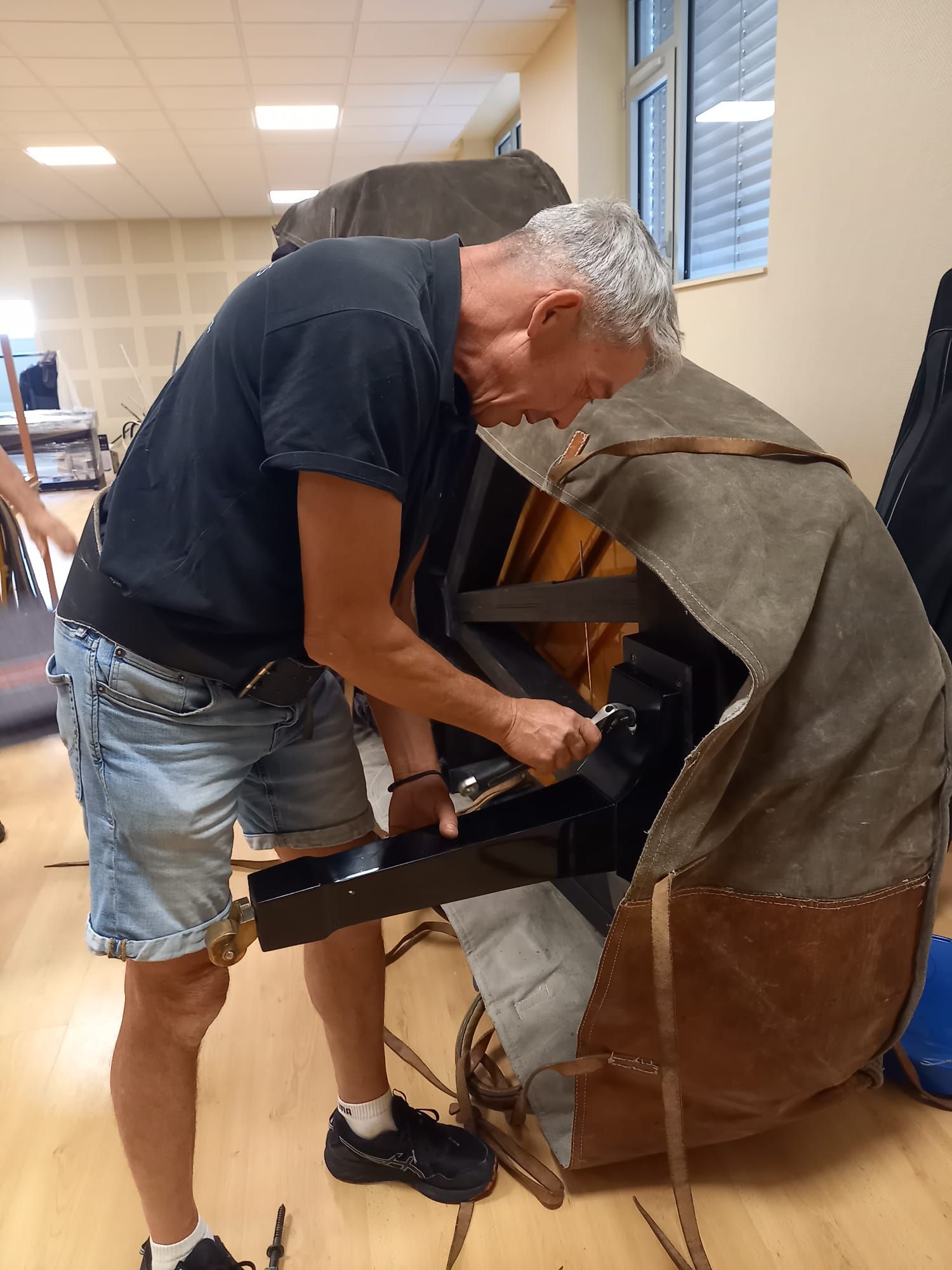 Un homme se penche sur un piano dans une pièce, en train d'en ajuster ou d'en réparer l'intérieur.