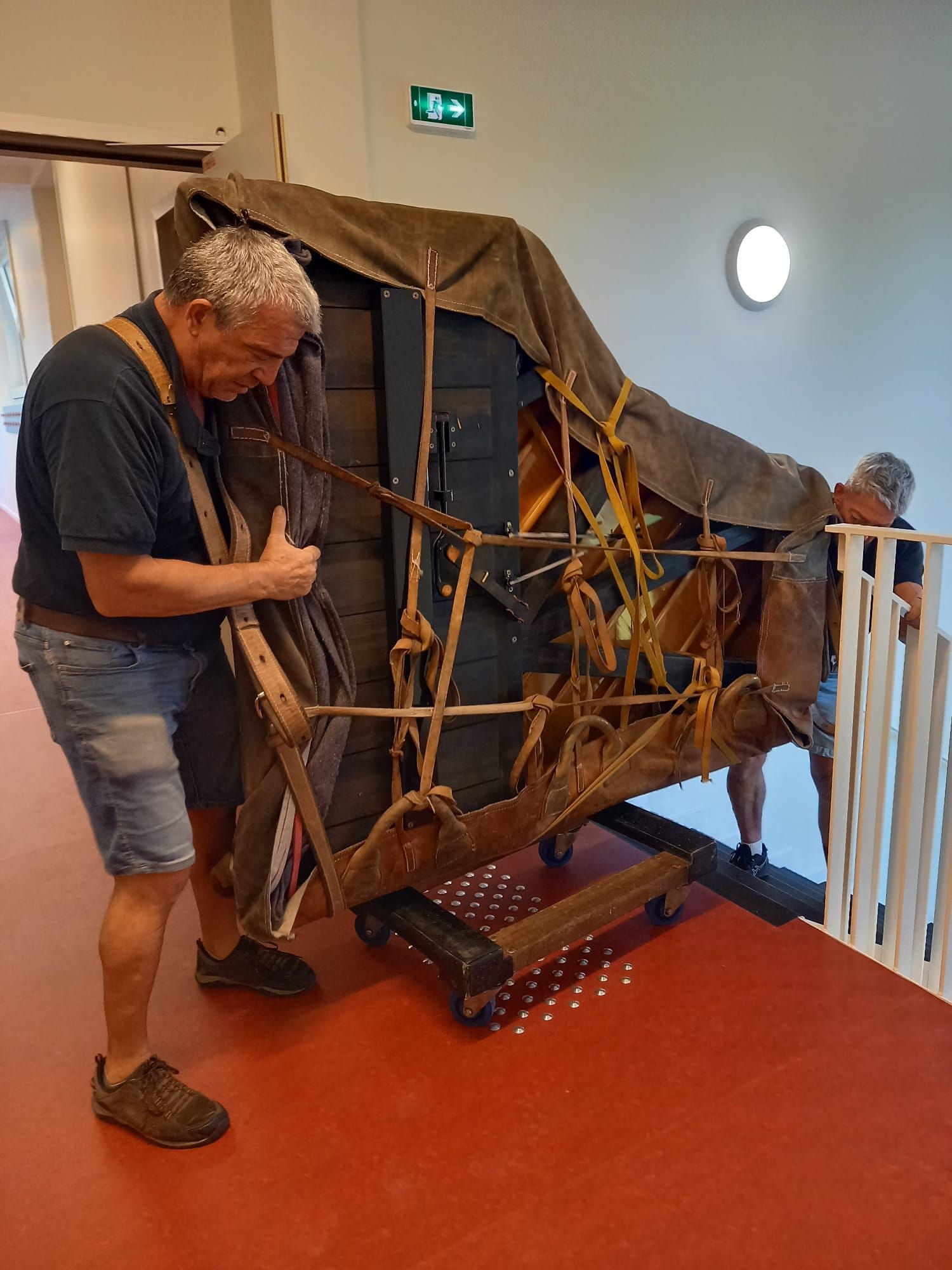 Un homme ajuste un gros objet recouvert, attaché à un chariot dans un couloir.